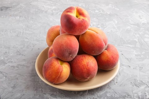 Fresh peaches on a plate on gray concrete background. side view, close up