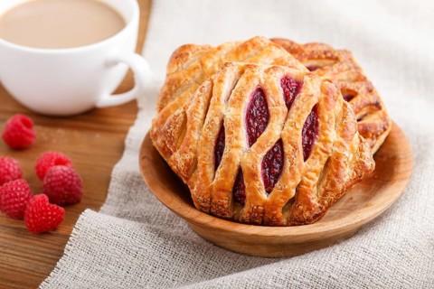 Puff pastry buns with strawberry jam on wooden background with linen textile and a cup of coffee.