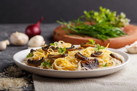Rice noodles with champignons mushrooms, egg sauce and oregano on white ceramic plate on a black