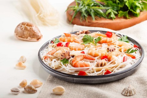 Rice noodles with shrimps or prawns and small octopuses on gray ceramic plate on a white wooden