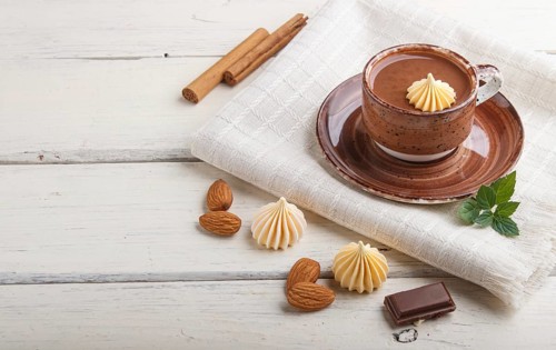 Cup of hot chocolate and pieces of milk chocolate with almonds on a white wooden background with