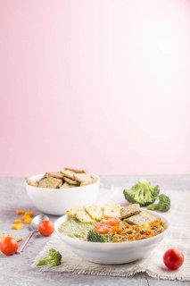 Green broccoli cream soup with crackers and cheese in white bowl on a gray and pink background and