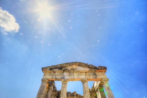 Sunshine pierces the ruins of an ancient temple with columns against a blue sky, Mausoleum, Heroon,