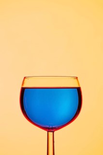 A clear wine glass with a calm blue liquid paired with a yellow background