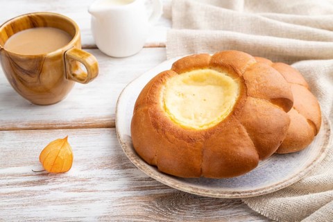Sour cream bun with cup of coffee on a white wooden background and linen textile. Side view, close
