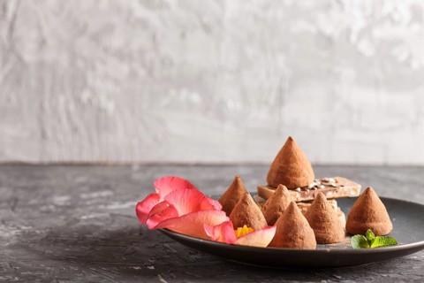 Chocolate truffle on blue ceramic plate decorated with rose petals on black concrete background.