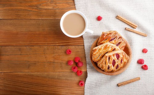 Puff pastry buns with strawberry jam on wooden background with linen textile and a cup of coffee.