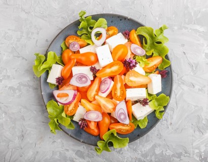 Vegetarian salad with fresh grape tomatoes, feta cheese, lettuce and onion on blue ceramic plate on
