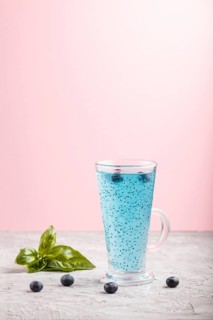 Glass of blueberry blue colored drink with basil seeds on a gray and pink background. Morninig,