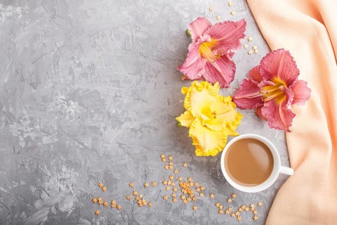 Yellow anf purple day-lilies cup of coffee on a gray concrete background, with orange textile.