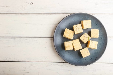 Traditional indian candy soan papdi in a blue ceramic plate with almond and pistache on a white