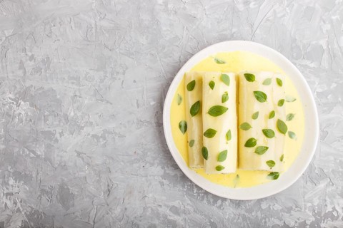 Cannelloni pasta with egg sauce, cream cheese and oregano leaves on a gray concrete background. top