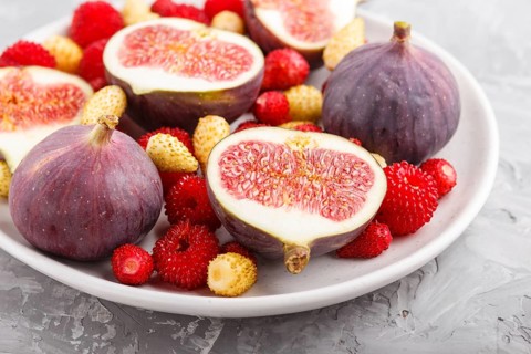 Fresh figs, strawberries and raspberries on white ceramic plate on gray concrete background. side