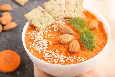 Carrot cream soup with sesame seeds, almonds and snacks in white bowl on a black concrete