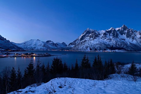 Blick auf verschneite Berge und einen Fjord in Norwegen waehrend der blauen Stunde, Lofoten