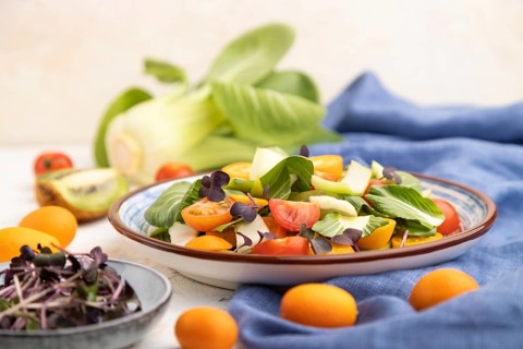 Vegetarian salad of pac choi cabbage, kiwi, tomatoes, kumquat, microgreen sprouts on a white