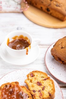 Homemade cake with raisins, almonds, soft caramel and a cup of coffee on a white wooden background.