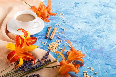 Orange day-lily and lavender flowers and a cup of coffee on a blue concrete background, with orange