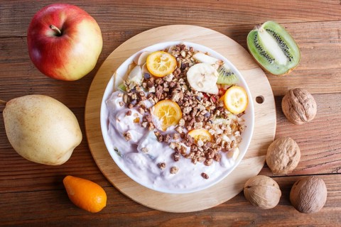 Vegetarian salad of bananas, apples, pears, kumquats, kiwi with granola and yogurt on brown woodem