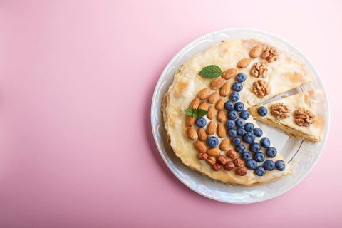 Homemade layered Napoleon cake with milk cream. Decorated with blueberry, almonds, walnuts,