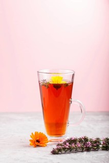 Glass of herbal tea with calendula and hyssop on a gray and pink background. Morninig, spring,