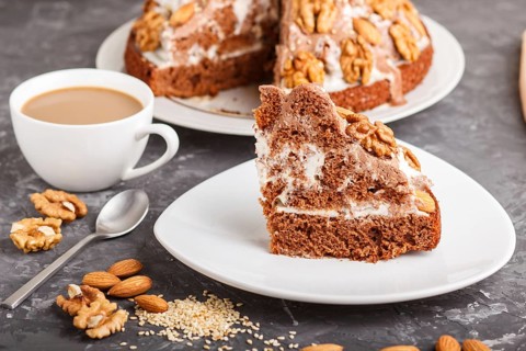 Homemade cake with milk cream, cocoa, almond, hazelnut on a black concrete background and a cup of