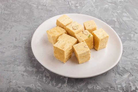Traditional indian candy soan papdi in white plate with almond and pistache on a gray concrete