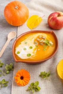 Traditional pumpkin cream soup with seeds in clay bowl on a gray concrete background with linen