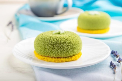 Green mousse cake with pistachio cream and a cup of coffee on a white wooden background and blue