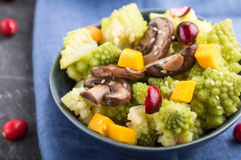 Vegetarian salad from romanesco cabbage, champignons, cranberry, avocado and pumpkin on a black