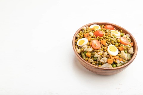 Mung bean porridge with quail eggs, tomatoes and microgreen sprouts on a white wooden background.