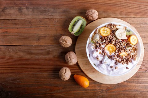 Vegetarian salad of bananas, apples, pears, kumquats, kiwi with granola and yogurt on brown woodem