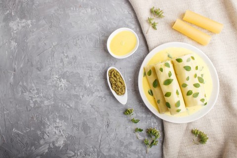 Cannelloni pasta with egg sauce, cream cheese and oregano leaves on a gray concrete background with