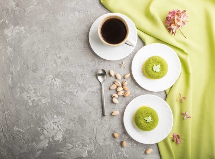 Green mousse cake with pistachio cream and a cup of coffee on a gray concrete background and green