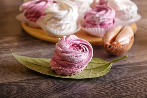 Pink and white homemade marshmallows (zephyr) on a round wooden board with seashells on a gray