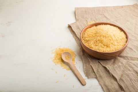Wooden bowl with raw golden rice and wooden spoon on a white wooden background and linen textile.