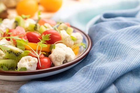Vegetarian salad of cauliflower cabbage, kiwi, tomatoes, microgreen sprouts on white wooden
