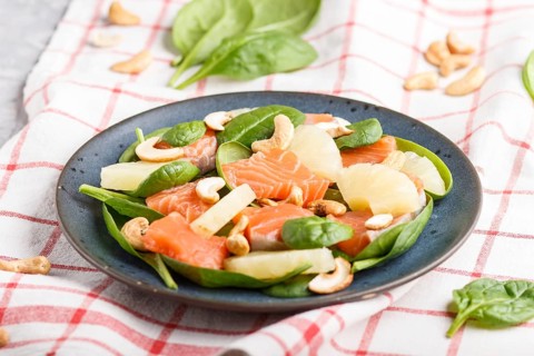 Fresh salmon with pineapple, spinach and cashew on a gray concrete background. Side view, close up,