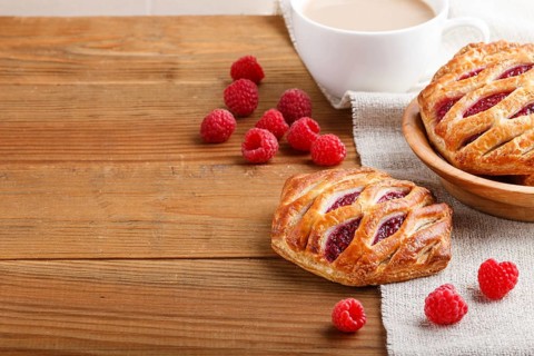 Puff pastry buns with strawberry jam on wooden background with linen textile and a cup of coffee.