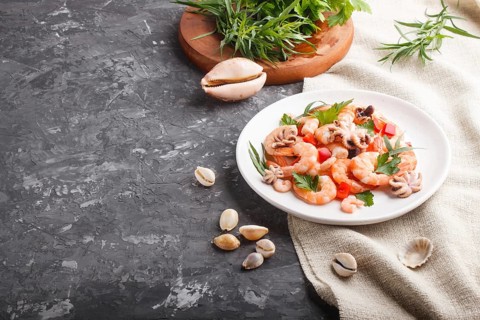 Boiled shrimps or prawns and small octopuses with herbs on white ceramic plate on a black concrete