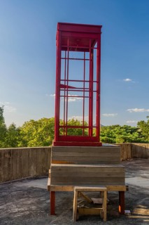 Red wooden telephone booth minus phone and without glass on roof of building on sunny day with blue