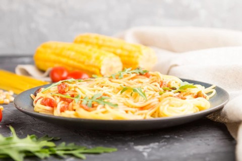 Corn noodles with tomato sauce and arugula on a black concrete background and linen textile. Side