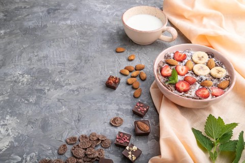 Chocolate cornflakes with milk, strawberry and almonds in ceramic bowl on gray concrete background