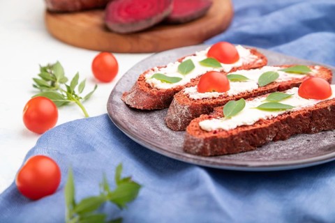 Red beet bread sandwiches with cream cheese and tomatoes on white concrete background and blue