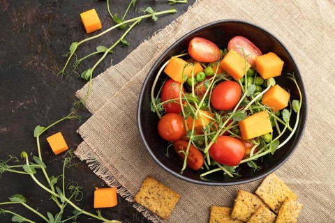 Vegetarian vegetable salad of tomatoes, pumpkin, microgreen pea sprouts on black concrete