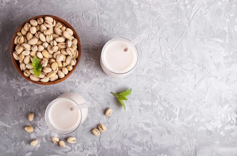 Organic non dairy pistachio milk in glass and wooden plate with pistachionuts on a gray concrete