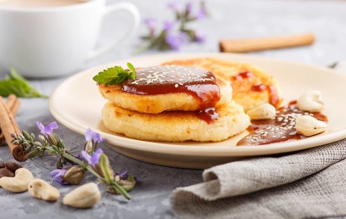 Cheese pancakes with caramel sauce on a beige ceramic plate and a cup of coffee on a gray concrete