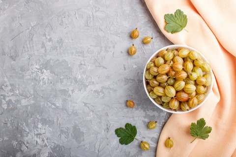 Fresh green gooseberry in white bowl with orange textile on gray concrete background. top view,