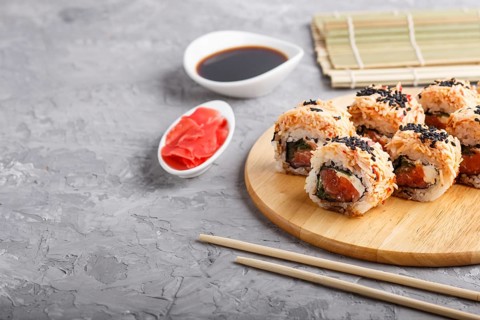 Japanese maki sushi rolls with salmon, sesame, chopsticks, soy sauce and marinated ginger on wooden