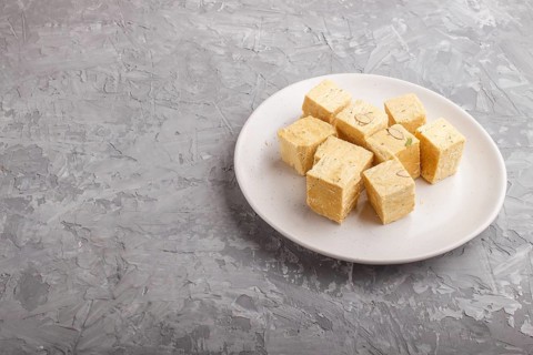 Traditional indian candy soan papdi in white plate with almond and pistache on a gray concrete